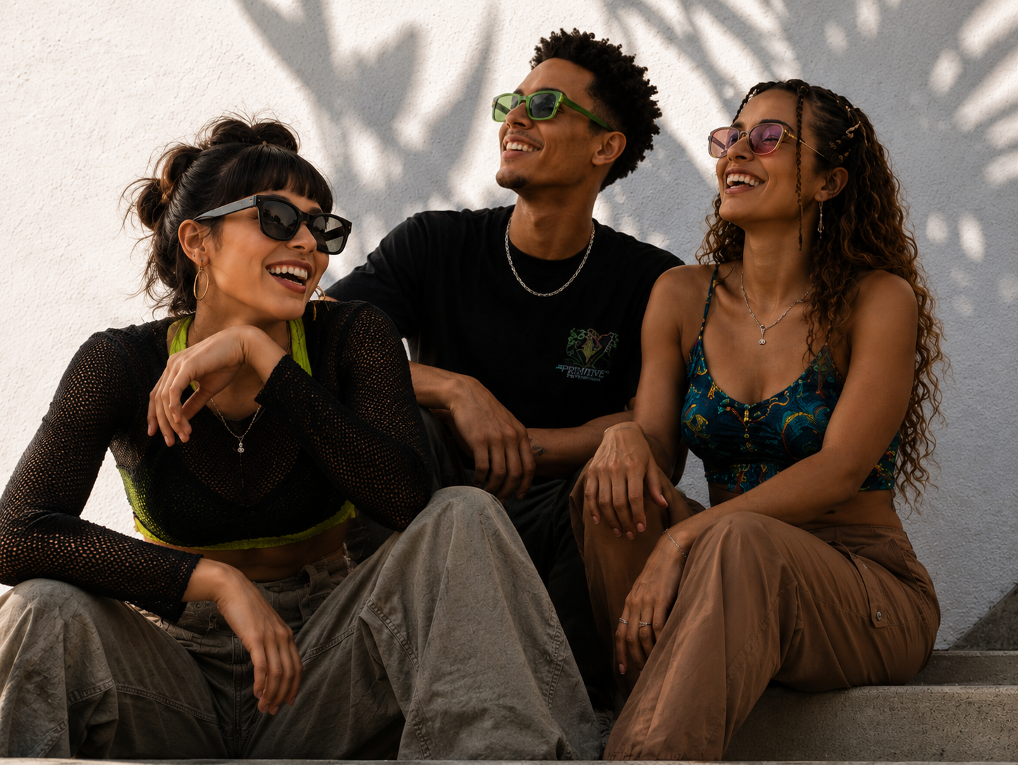 Three friends in sunglasses laughing together on sunlit steps under palm shadows